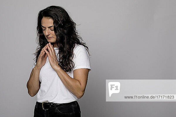 Contemplating woman with hands clasped standing against gray background