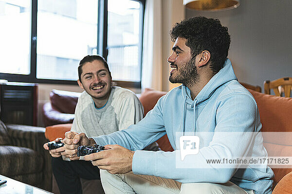 Lächelnde junge Freunde  die sich beim Spielen eines Videospiels zu Hause unterhalten