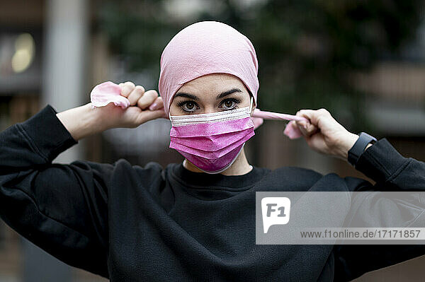 Female cancer patient in bandana wearing pink protective face mask during COVID-19