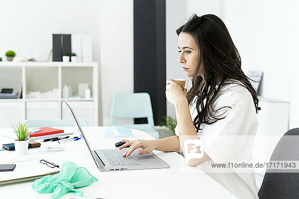 Ärztin beim Kaffee trinken und Online-Beratung am Schreibtisch in der Klinik