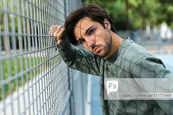 Handsome man leaning on fence of basketball court
