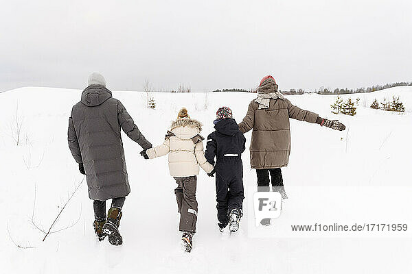 Eltern mit Kindern spazieren auf schneebedeckter Landschaft gegen den Himmel