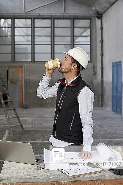 Männlicher Architekt trinkt Kaffee  während er an einem Tisch in einem Gebäude steht