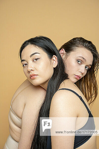 Multi-ethnische weibliche Modelle in Dessous lehnen sich gegenseitig auf die Schulter vor gelbem Hintergrund