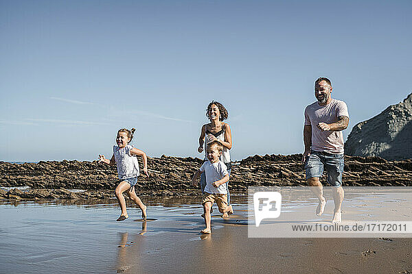 Cheerful family running at beach against sky
