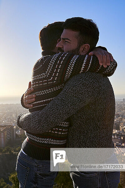 Loving gay men embracing while standing against clear sky during sunrise  Bunkers del Carmel  Barcelona  Spain