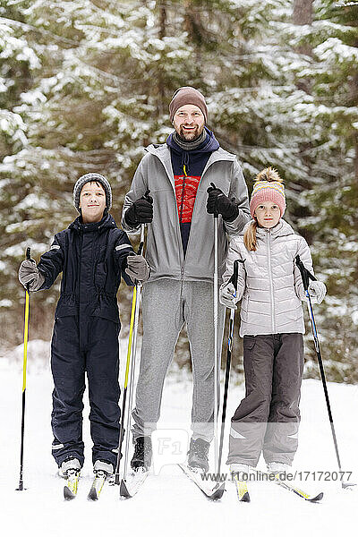 Vater und Kinder beim Skifahren gegen Bäume im verschneiten Wald