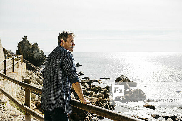 Älterer Mann lehnt sich an die Reling und blickt auf das Meer an einem sonnigen Tag