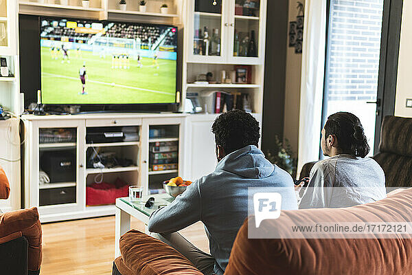 Junge männliche Freunde spielen Fußball vor dem Fernseher im heimischen Wohnzimmer