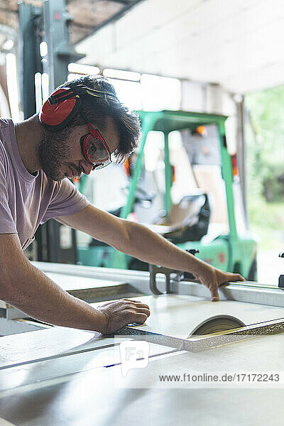 Young male craftsperson cutting wood using table saw in workshop