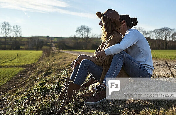 Heterosexual couple sitting on field during sunset
