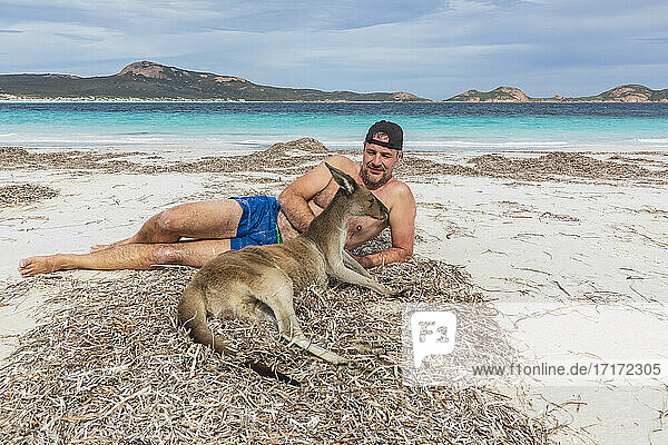 Mann mit Westlichem Grauen Känguru am Strand liegend  Westaustralien