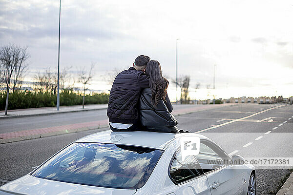 Young man sitting with woman on car rooftop