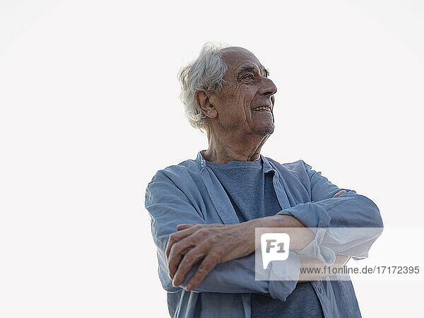 Älterer Mann mit verschränkten Armen  der lächelnd vor dem Himmel steht