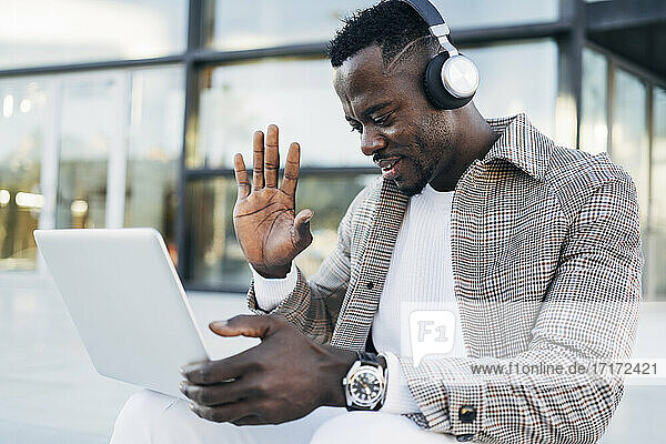 Mann trägt Kopfhörer und gestikuliert bei einem Videotelefonat mit einem Laptop