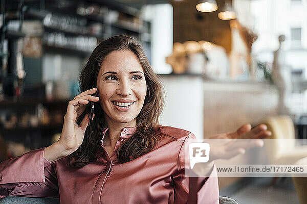 Lächelnde weibliche Freiberuflerin gestikuliert  während sie mit ihrem Smartphone in einem Café spricht