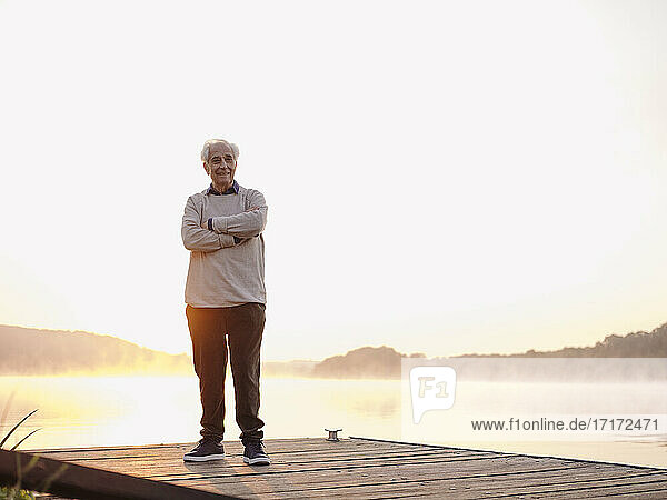 Mann lächelt  während er mit verschränkten Armen auf dem Pier steht