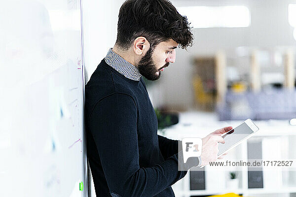 Geschäftsmann  der ein digitales Tablet vor einem Whiteboard im Büro benutzt