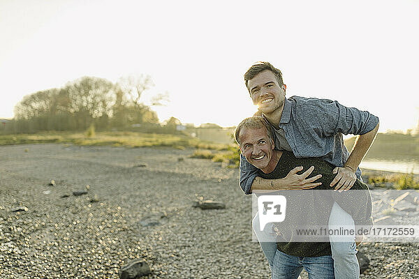 Smiling father giving piggyback ride to son against clear sky at evening