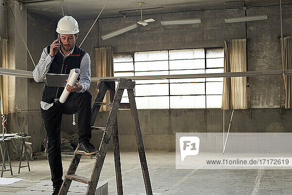 Male architect discussing over mobile phone while using digital tablet in building