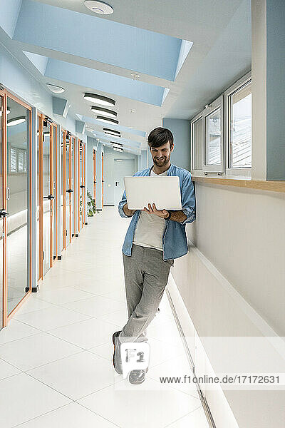 Male professional working on laptop in office corridor