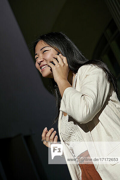 Smiling young woman talking on smart phone during sunny day