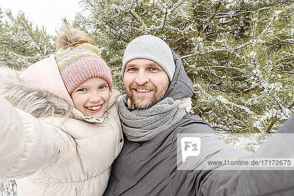 Smiling father and daughter against trees in forest during winter