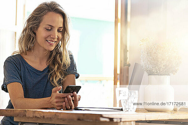 Smiling female freelancer using mobile phone at home office