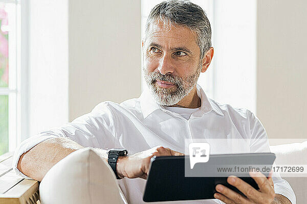 Geschäftsmann mit digitalem Tablet  der wegschaut  während er zu Hause sitzt
