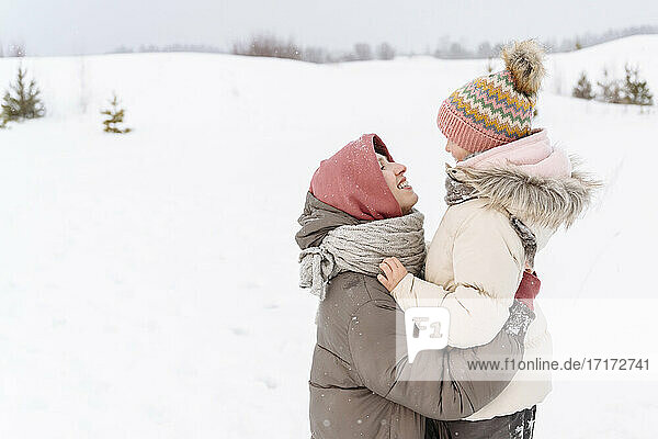 Smiling mother embracing daughter on snow covered landscape