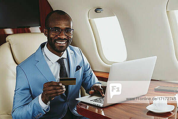 Lächelnder Geschäftsmann mit Kredit und Laptop im Privatjet