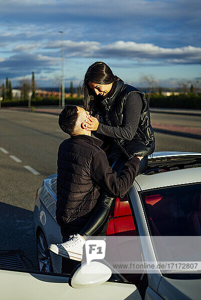 Young man doing romance with woman sitting on car