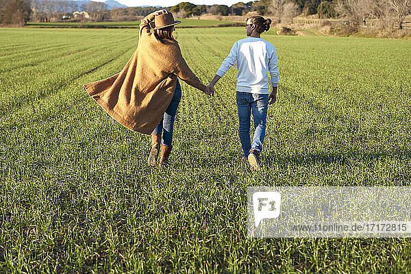 Woman holding boyfriend's hand while walking on grass during sunset