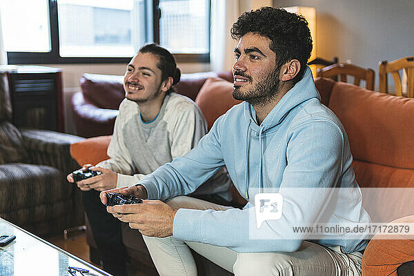 Male friends enjoying video game while sitting on sofa in living room