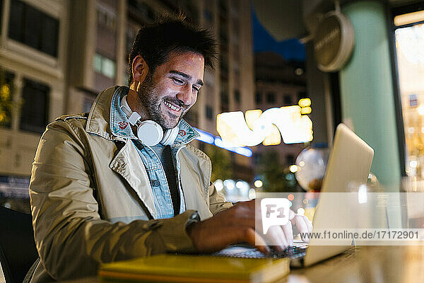 Smiling man using laptop while sitting at sidewalk cafe