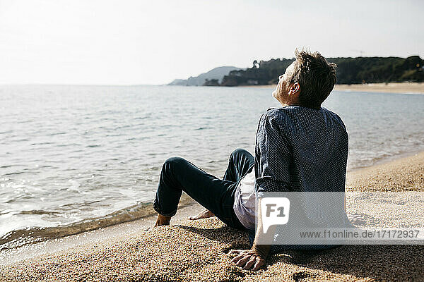 Entspannter Mann  der am Strand sitzt  an einem sonnigen Tag