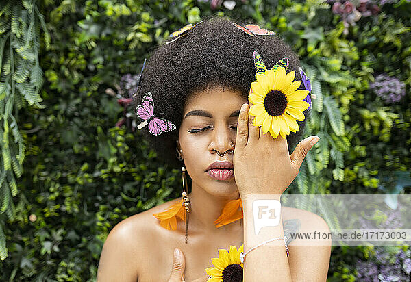 Afro woman covering eye with hand against plant