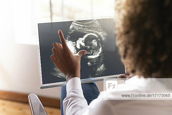 Frau betrachtet Ultraschallbild des Babys auf transparentem Bildschirm, während sie zu Hause sitzt