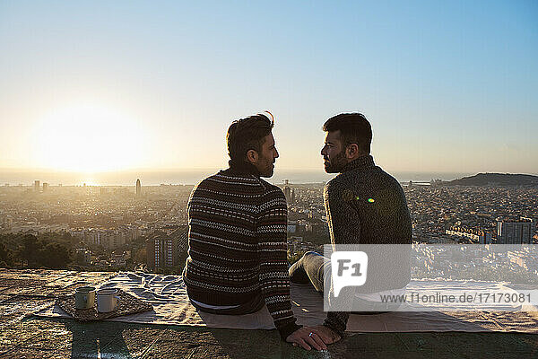 Homosexuelles Paar  das sich während des Sonnenaufgangs auf dem Aussichtspunkt sitzt  Bunkers del Carmel  Barcelona  Spanien