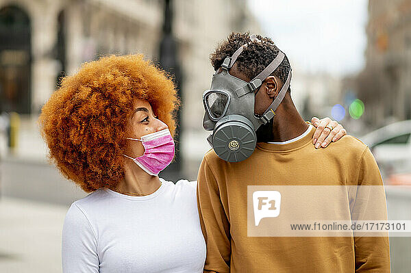 Couple wearing protective face mask looking at each other while standing outdoors