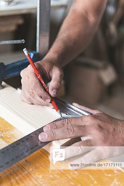 Young male carpenter marking on wood using pencil and ruler while working in workshop