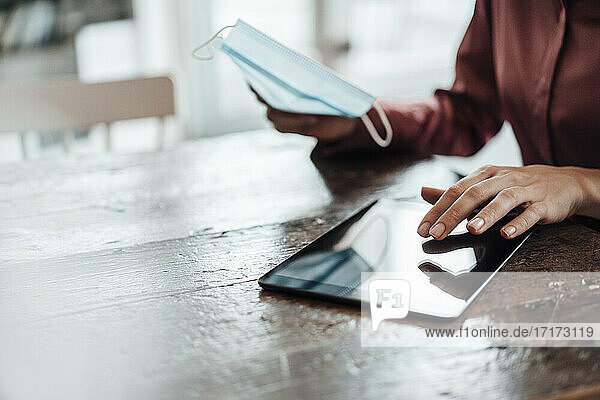 Die Hand einer Unternehmerin  die während der Pandemie ein digitales Tablet am Tisch eines Cafés benutzt