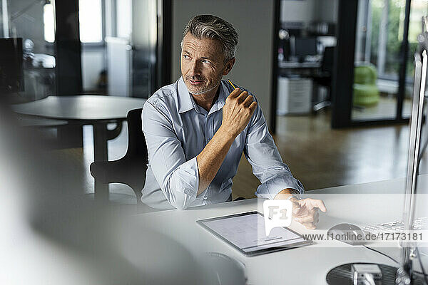 Nachdenklicher Geschäftsmann schaut weg  während er am Schreibtisch im Büro sitzt