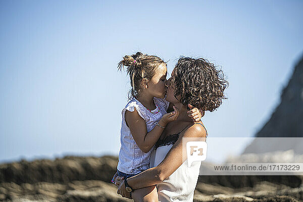 Mother and daughter kissing at flysch against blue sky