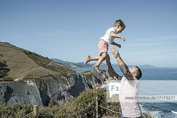 Father catching son at observation point against blue sky on sunny day