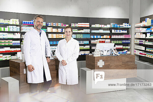Male with female pharmacist standing against pharmacy checkout in store