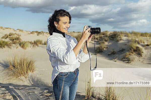 Smiling woman photographing through vintage camera while standing against cloudy sky