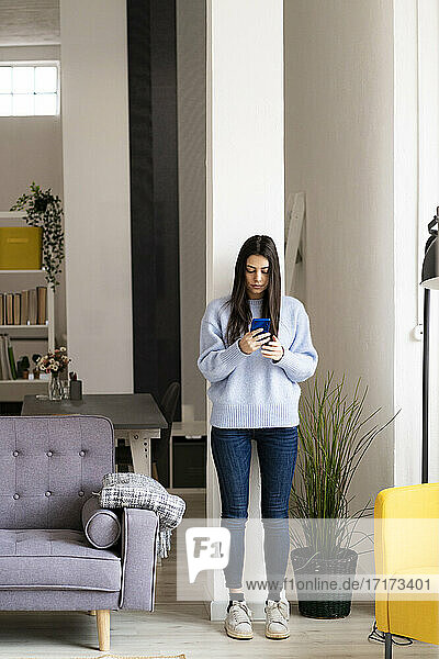 Young woman using mobile phone while standing at home