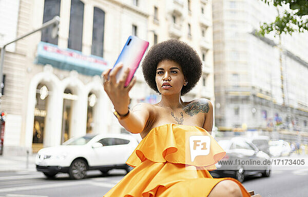 Afro woman taking selfie through mobile phone in city