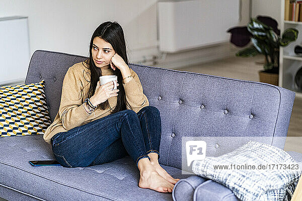 Thoughtful woman with coffee cup looking away while sitting at home